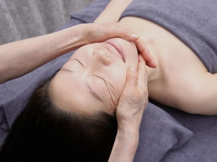 ベッドに横たわる女性のフェイスラインを施術する手元